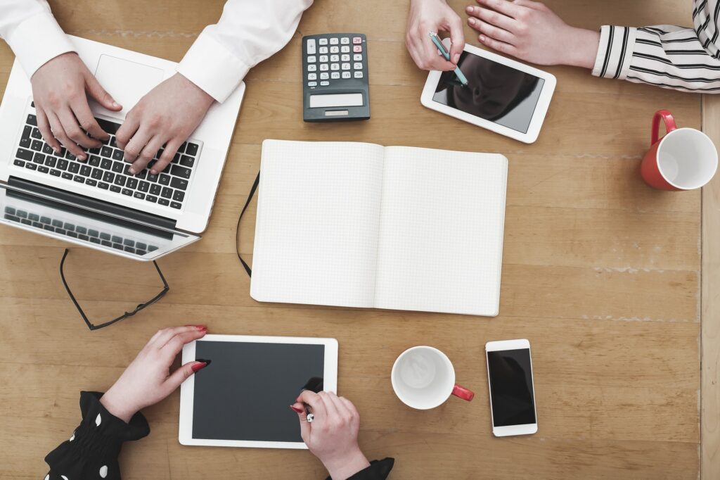 Young business team working together as a group on office desk with multiple electronic devices and